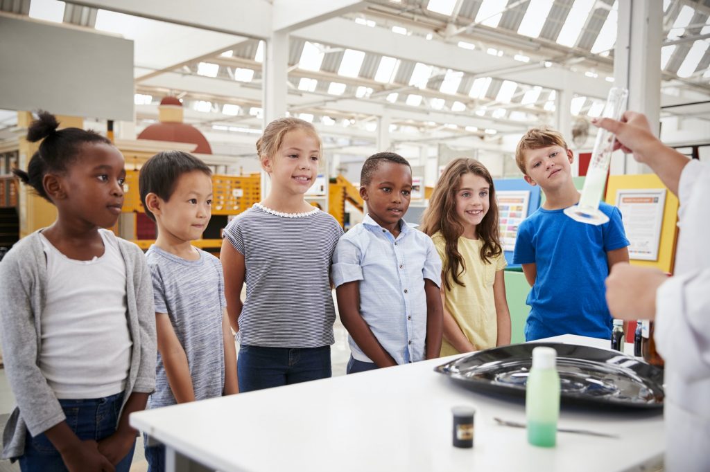 Lab technician showing graduated cylinder to a group of kids